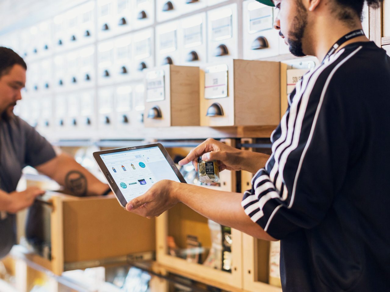 Dos personas trabajan junto a las estanterías de un depósito consultando una tablet.