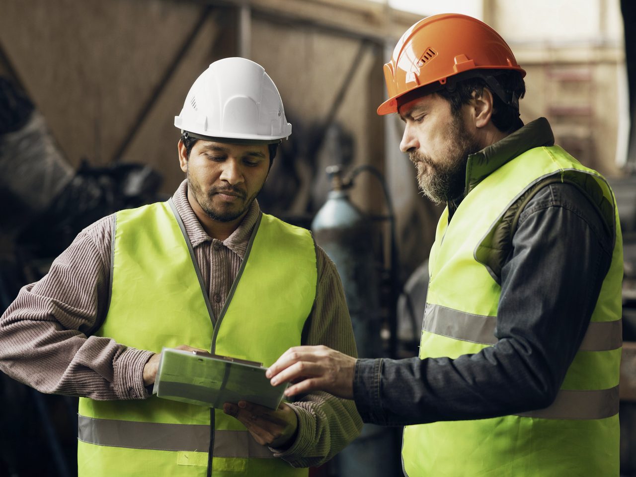 Dos profesionales con chaleco y casco conversan en una planta industrial.